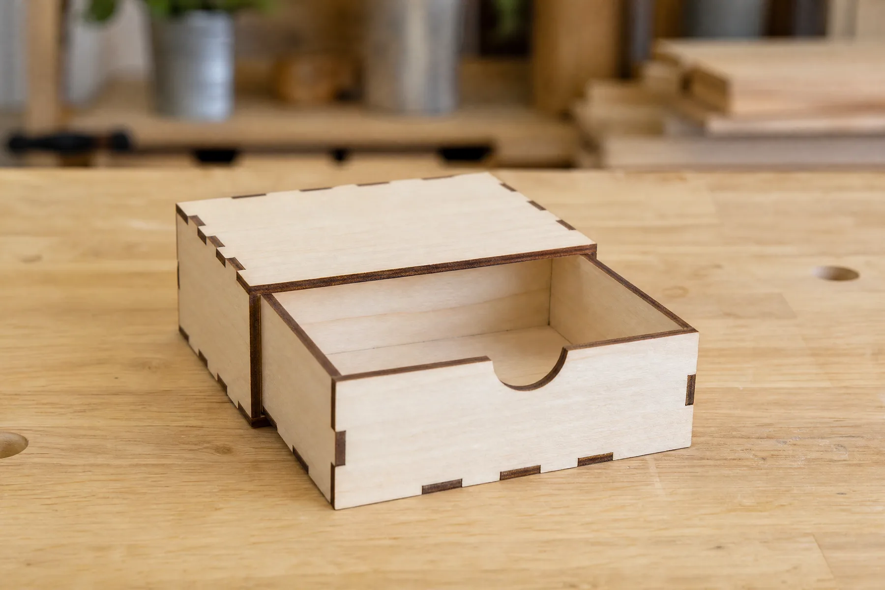 A laser-cut wooden drawer with a finger hole sliding out of its sleeve, both with finger joints